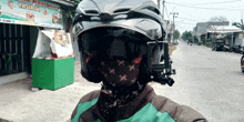 a man wearing a helmet and a bandana stands in front of a sign that says ' wisata ' on it