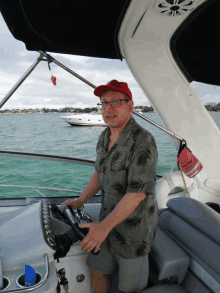 a man wearing a red hat and glasses is driving a boat in the ocean