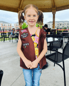 a little girl wearing a brown vest that says girl scouts of the usa