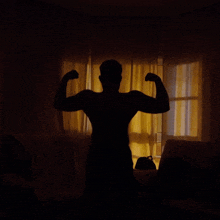 a silhouette of a man flexing his arms in front of a window