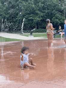 a little girl sits in a fountain while a woman stands behind her