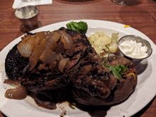 a white plate topped with a steak and vegetables with a side of sour cream