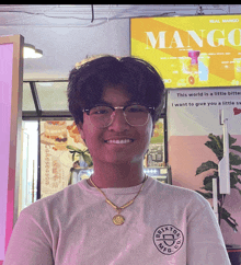 a young man stands in front of a sign that says " mango " on it