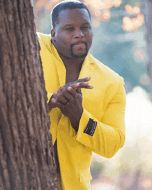 a man in a yellow suit is peeking out from behind a tree with his hands folded