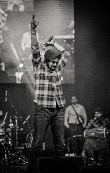 a man in a plaid shirt is standing on a stage holding a microphone in his hand .