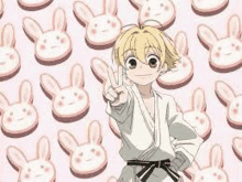 a boy in a karate uniform is giving a peace sign in front of a pattern of bunny cookies .