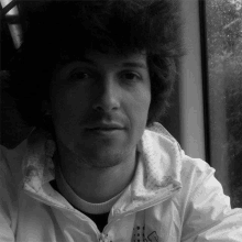 a man with curly hair is wearing a white jacket and looking out of a window .