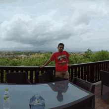 a man standing on a balcony wearing a red shirt that says gnk on it