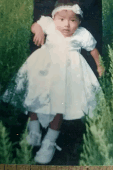 a little girl in a white dress is standing in the grass