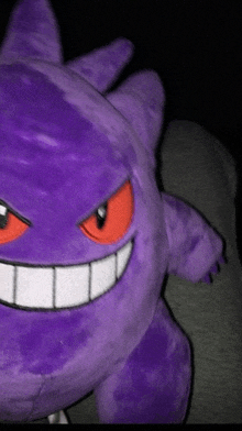 a close up of a purple stuffed animal with red eyes and white teeth