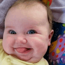 a baby is smiling with his tongue hanging out while laying in a crib .