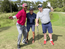 three men are posing for a picture on a golf course with one wearing a pink shirt with the letter o on it