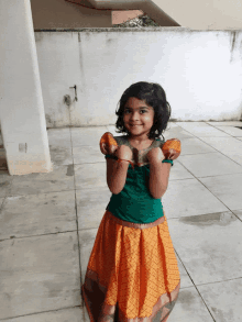 a little girl wearing a green top and orange skirt stands on a tiled floor