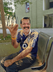 a man wearing a shirt with the letter d on it is sitting on a bench and smiling