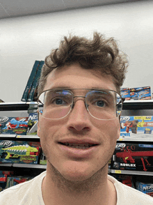 a man wearing glasses is smiling in front of a shelf with nerf toys