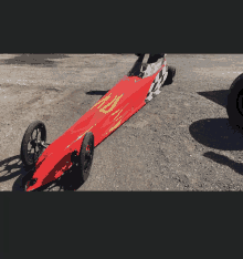 a red dragster with flames painted on the side is parked on a gravel road