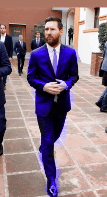 a man in a purple suit and tie walks down a brick sidewalk