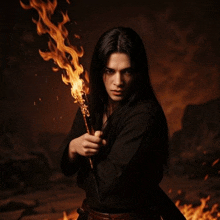 a man with long black hair is holding a torch with flames on it