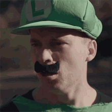 a man wearing a green hat with the letter l on it and a fake mustache