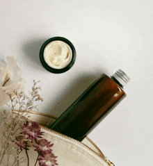 a bottle of cream sits next to a jar of cream and flowers