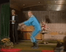 a man in a blue suit is dancing on a stage while another man in a tuxedo stands behind him .