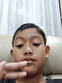 a young boy sitting on a couch making a peace sign with his finger