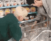 two men are shopping in a grocery store and one of them is looking at a cart filled with food .