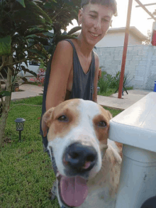 a woman stands next to a brown and white dog with its tongue hanging out