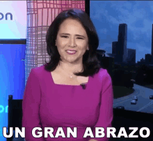 a woman in a purple dress is smiling in front of a sign that says " un gran abrazo "