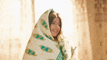 a woman is wrapped in a blanket and smiling while standing in front of a window .