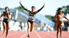 a group of women are running on a track and one of them is giving a peace sign .