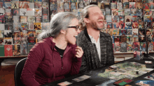 a man and a woman are laughing while playing a board game in front of a wall full of comic books