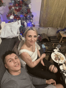 a man and woman sit on a couch in front of a christmas tree with a bag that says " look " on it