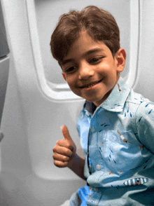 a young boy giving a thumbs up while sitting in an airplane