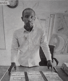 a black and white photo of a man sitting at a desk with a clock behind him that says " endiz " on it