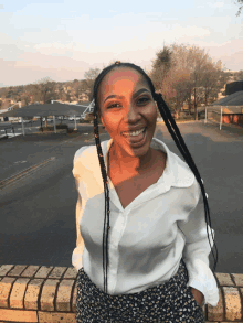 a woman wearing a white shirt and floral pants smiles in front of a parking lot