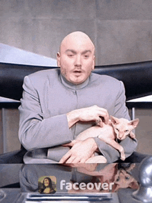 a bald man is holding a cat in his arms and the word faceover is on the table in front of him