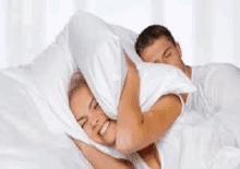 a woman is covering her ears with a pillow while a man sleeps next to her .