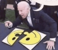 a man in a suit is sitting at a table with a smiley face cut in half .