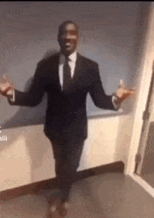 a man in a suit and tie is dancing with his arms outstretched in a hallway .