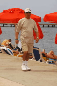 a man wearing sunglasses and a nike hat walks on the beach