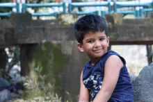 a young boy wearing a blue tank top is smiling for the camera