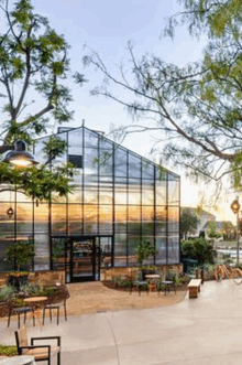 a greenhouse with tables and chairs in front of it and trees in the background .