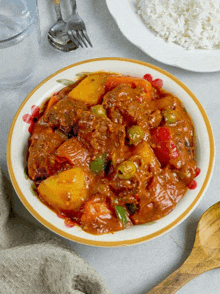 a bowl of stew with potatoes and peppers is next to a plate of rice