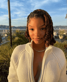 a woman wearing a white sweater and a diamond necklace looks at the camera