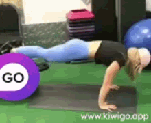 a woman is doing push ups on a yoga mat in a gym with a purple circle in the background .