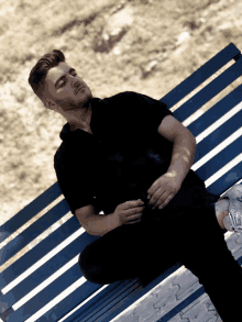 a man in a black shirt is sitting on a blue striped bench