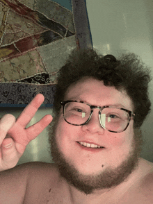 a shirtless man wearing glasses and a beard is giving a peace sign