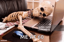 a skeleton is laying on a desk looking at a laptop computer .