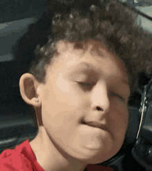 a young boy with curly hair and earrings is making a funny face .